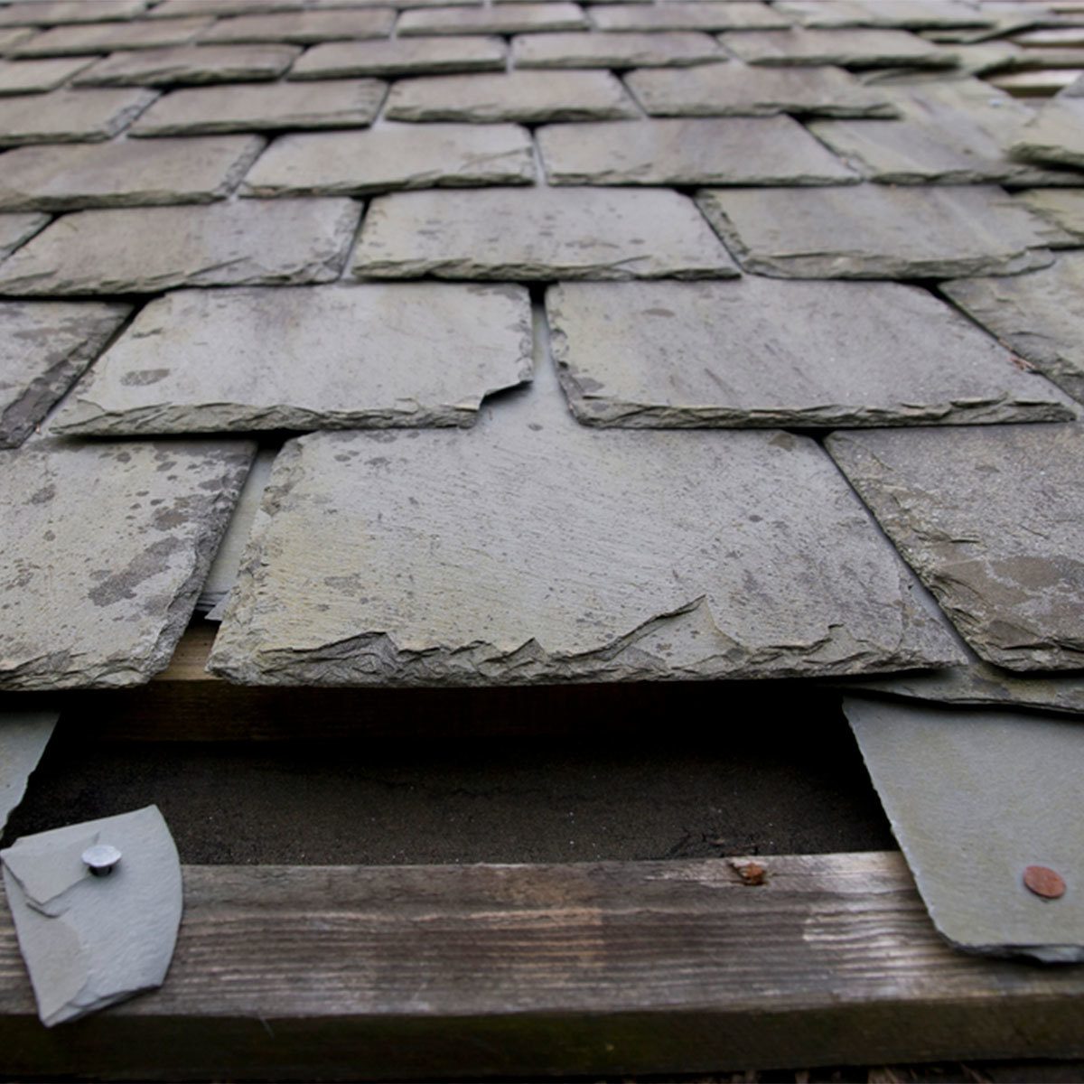 Slate tiles are arranged on a wooden structure, some slightly misaligned, indicating installation or repair of a roof in an outdoor setting.