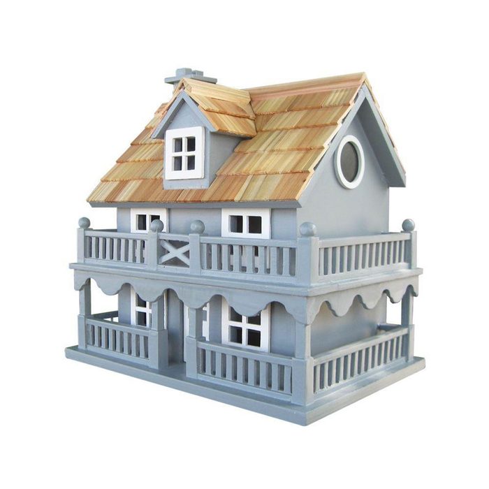 A gray toy house with a wooden roof and balconies sits on a flat surface, featuring multiple windows and decorative edges.