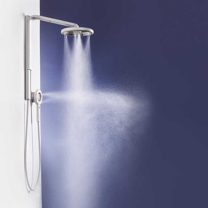A modern showerhead sprays water in a fine mist, mounted on a sleek wall, with a dark blue background enhancing the contemporary design.