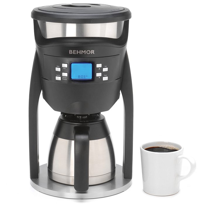 A coffee maker brews coffee, displayed next to a filled white mug on a gray base, showcasing a digital clock and control panel.