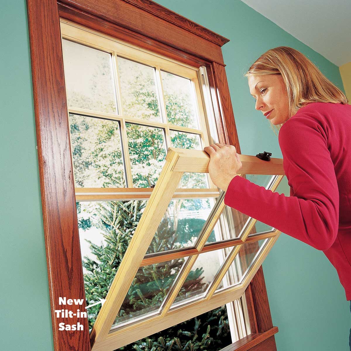 A woman tilts a window sash inward, revealing greenery outside, against a backdrop of a wooden window frame and a painted wall.