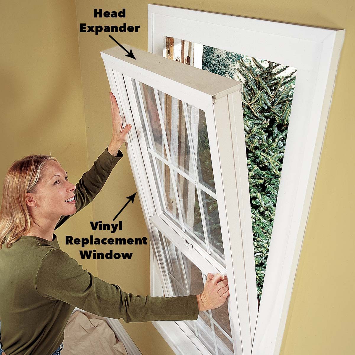 A woman installs a vinyl replacement window, adjusting it with a head expander, while a green tree is visible outside against a yellow wall.