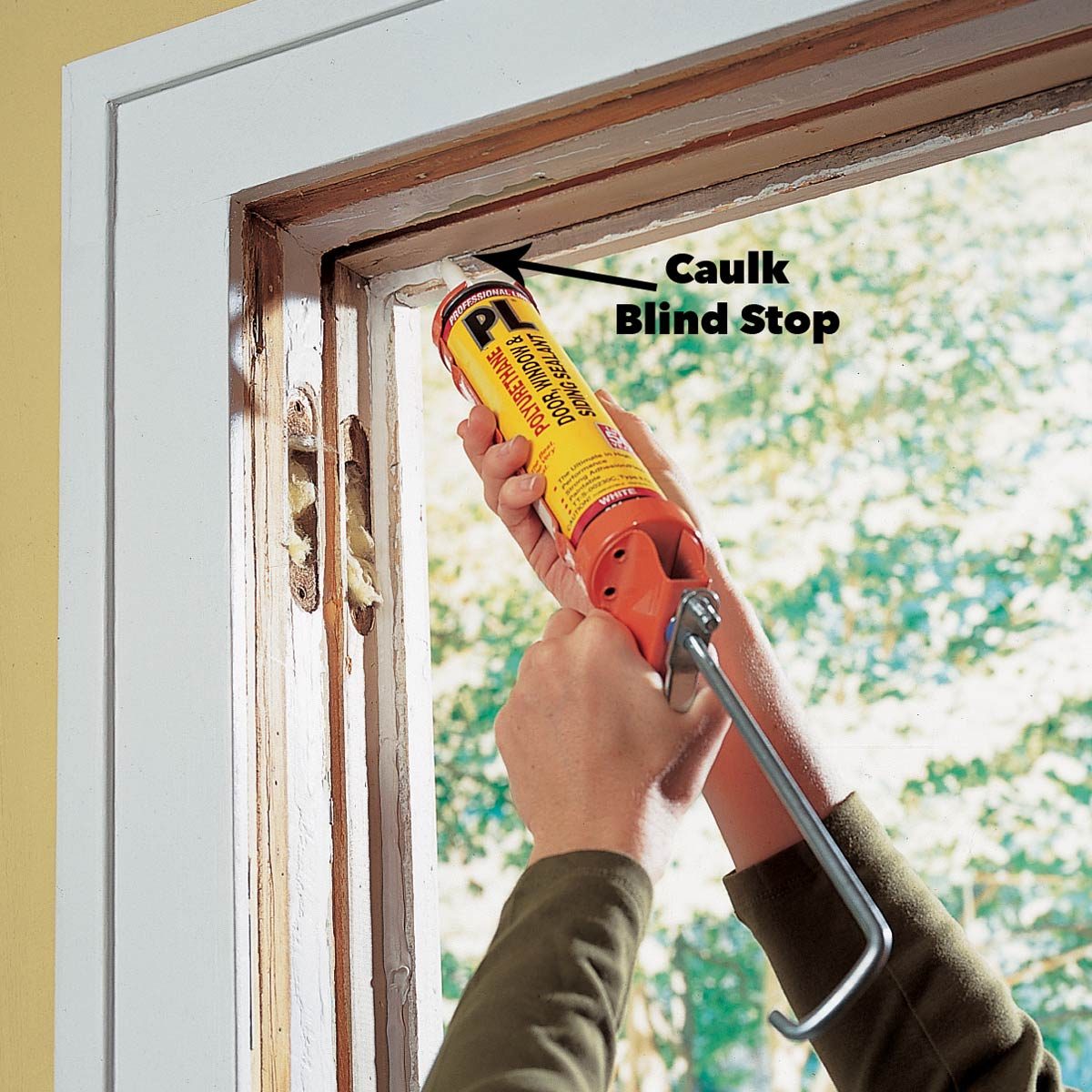 A person uses a caulking gun to apply caulk around a window frame, while sunlight streams in, illuminating the layered wooden structure.