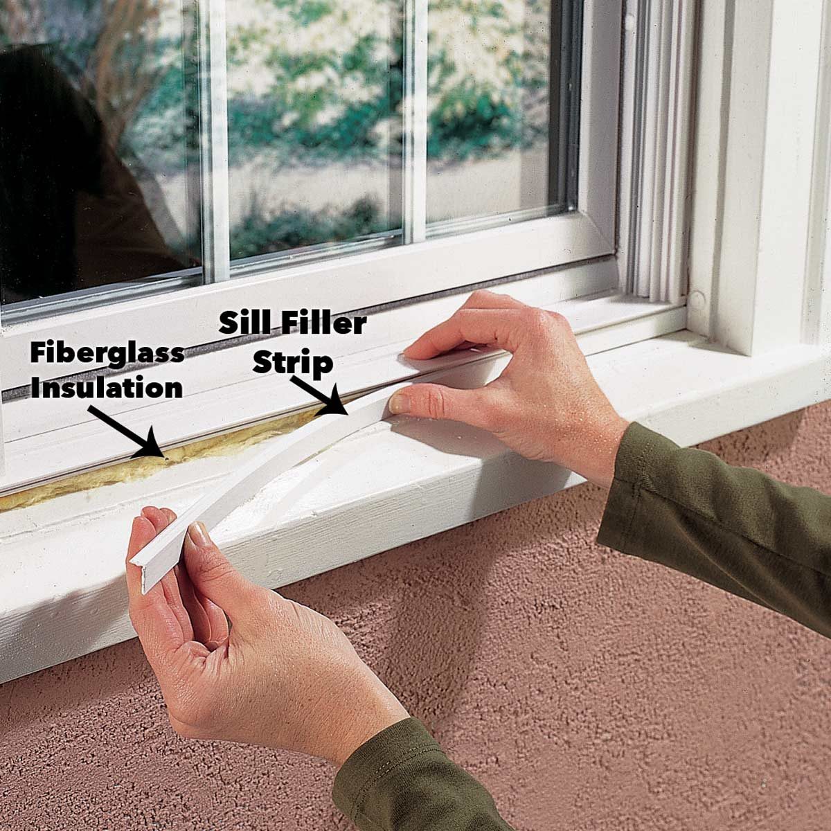 A hand applies a Sill Filler Strip over fiberglass insulation at a window's bottom edge, with a blurred outdoor view in the background.