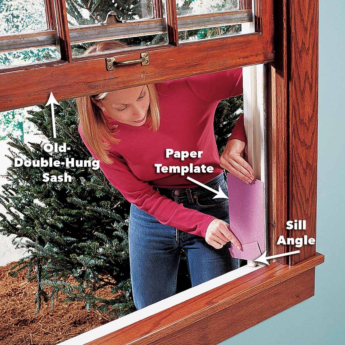 A woman is placing a paper template against a window frame while surrounded by a Christmas tree and wooden window finishes in a home interior.