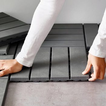 A person arranges gray interlocking floor tiles on a surface, focusing on aligning them correctly in a well-lit, indoor space.