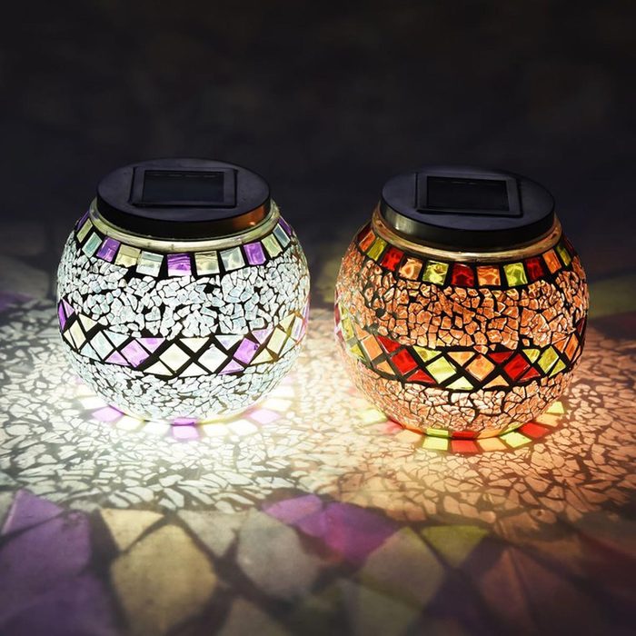 Two mosaic solar-powered lanterns glow gently, casting colorful shadows on a dark surface, creating a warm, decorative ambiance.