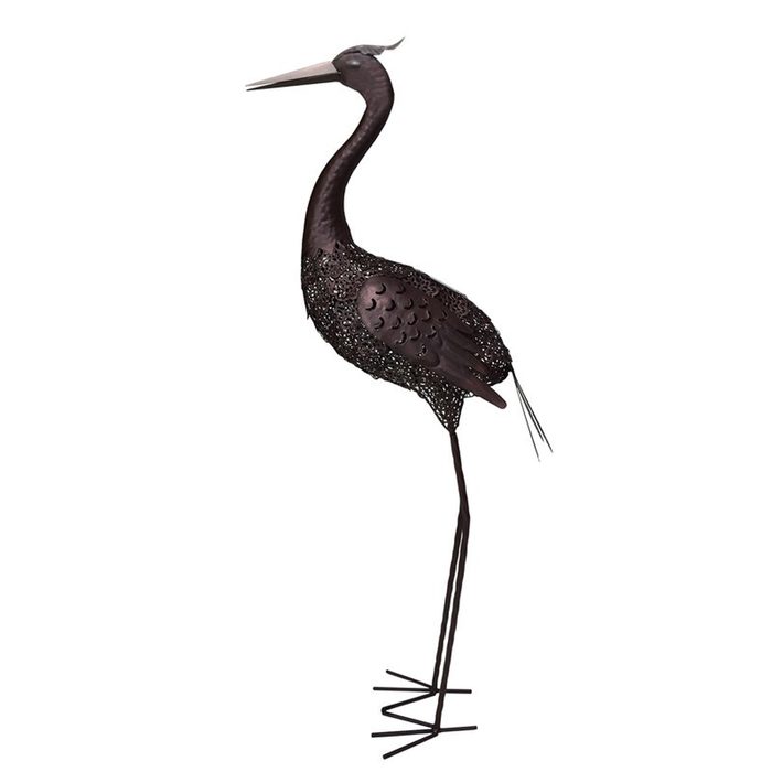 A metal heron sculpture stands upright, its long legs supporting an intricately detailed body, evoking a stylized representation of the bird.