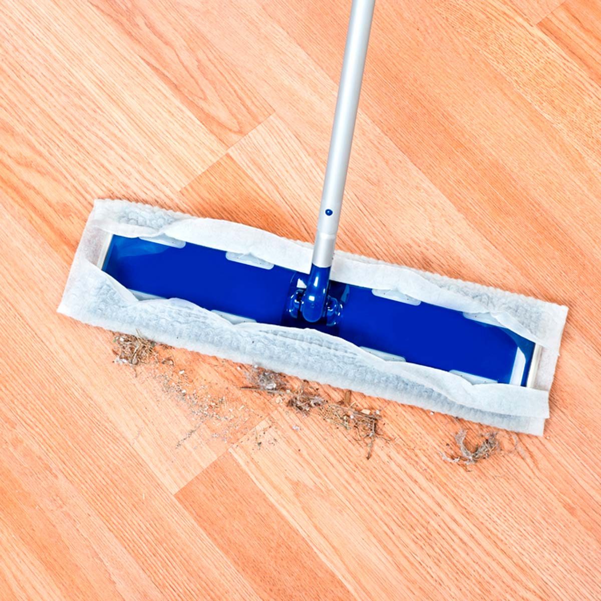 A blue cleaning mop is sweeping dirt and debris across a wooden floor, showcasing an effective cleaning action in a tidy domestic environment.