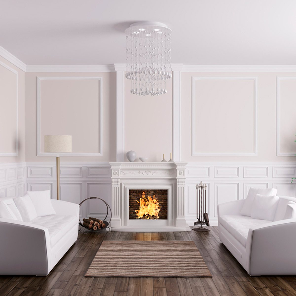 A white sofa sits opposite another, facing a cozy fire in a decorative fireplace. A chandelier hangs above, illuminating the elegant, light-colored room.