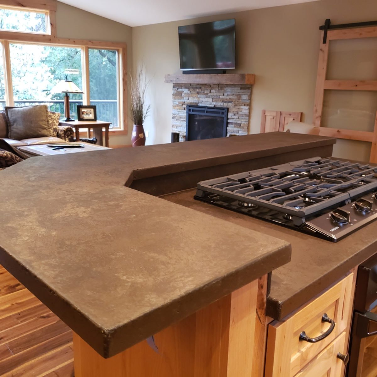 A modern kitchen counter with a gas stove is positioned prominently, featuring wooden cabinetry and a cozy living area in the background, including a fireplace and TV.