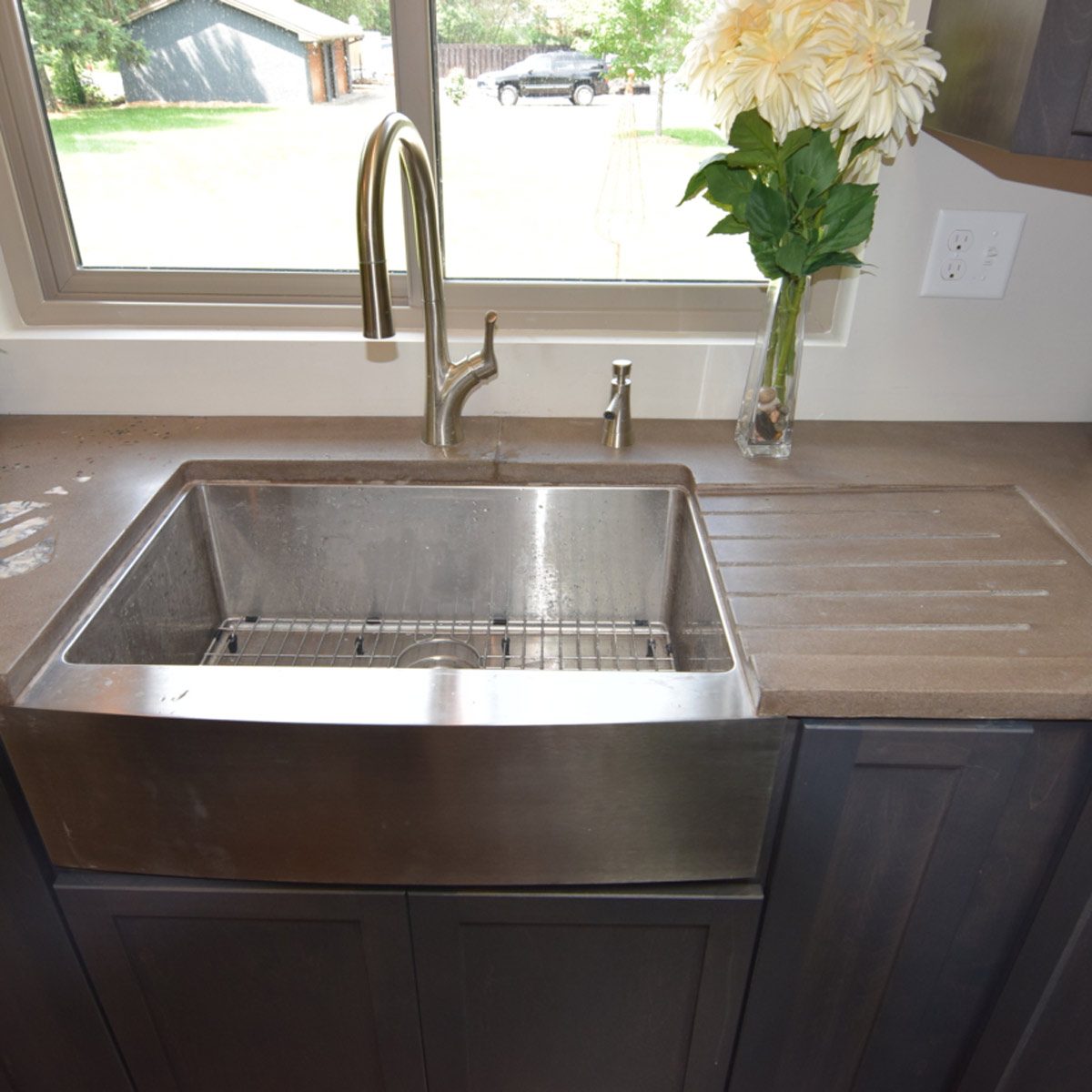 A stainless steel sink with a modern faucet is positioned on a countertop, accompanied by a decorative vase of flowers and a clear view of the outdoors.