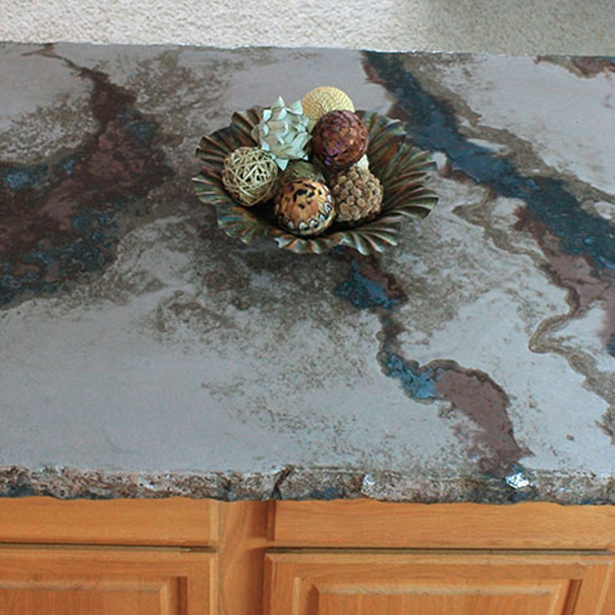 A decorative bowl sits on a patterned countertop, filled with various textured ornaments, surrounded by a plain backdrop.
