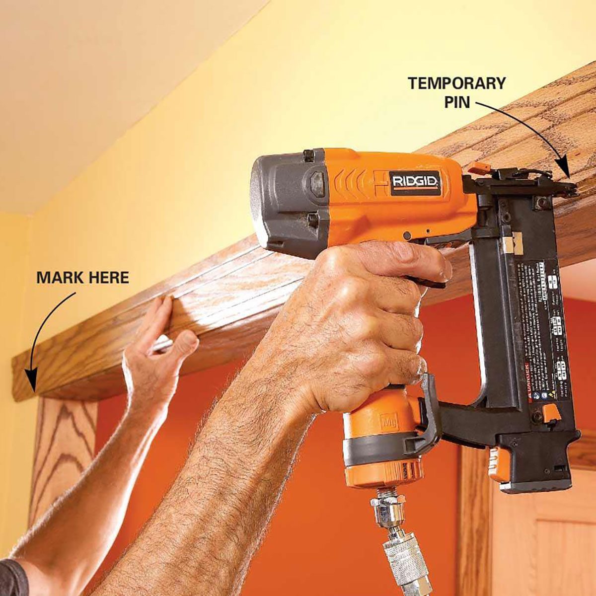 A hand holds a nail gun, attaching a wooden beam to a wall, marked for placement, in a brightly colored room.
