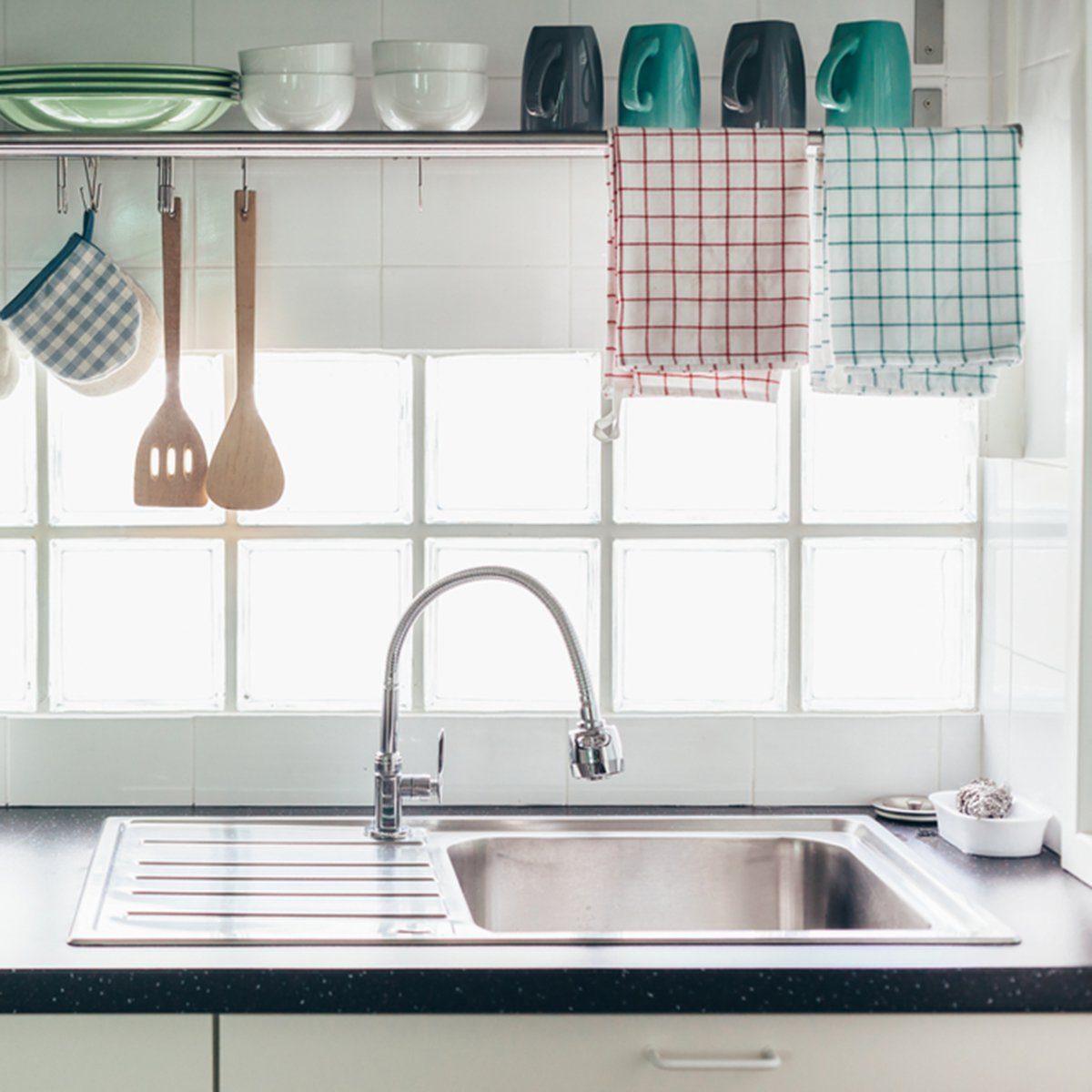 Home kitchen interior. Cooking utensils on a railing system and shelf with dishes above a window.; Shutterstock ID 698380921