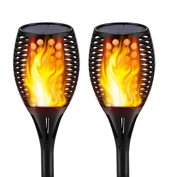 Two solar-powered torches emit a flickering flame effect, standing upright in a dark outdoor setting, creating a warm, inviting atmosphere.