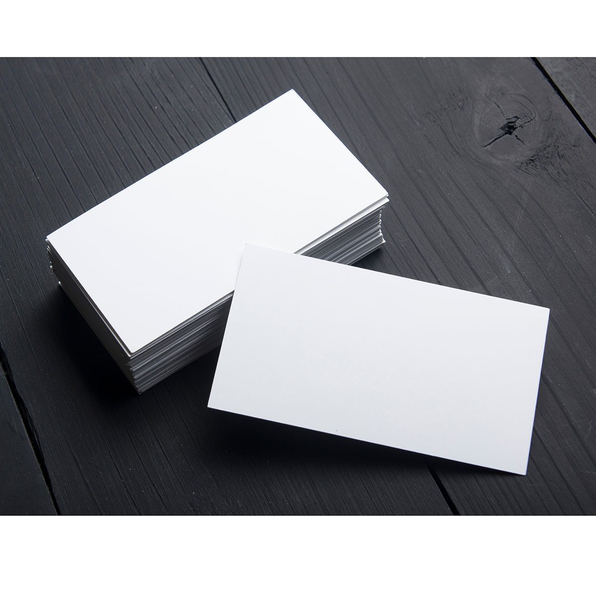 A stack of blank white cards sits on a dark wooden surface, with one card partially out of the stack, positioned horizontally.