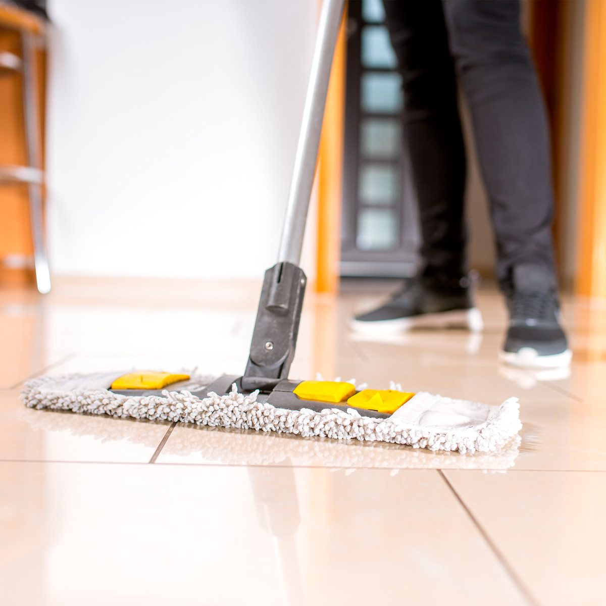 A mop, with a dirty cleaning pad, is being used to clean a shiny tiled floor in a well-lit indoor space.