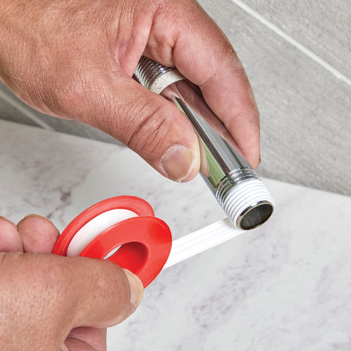 A hand applies white tape to a metal pipe's threaded end on a light surface, preparing it for a secure connection.