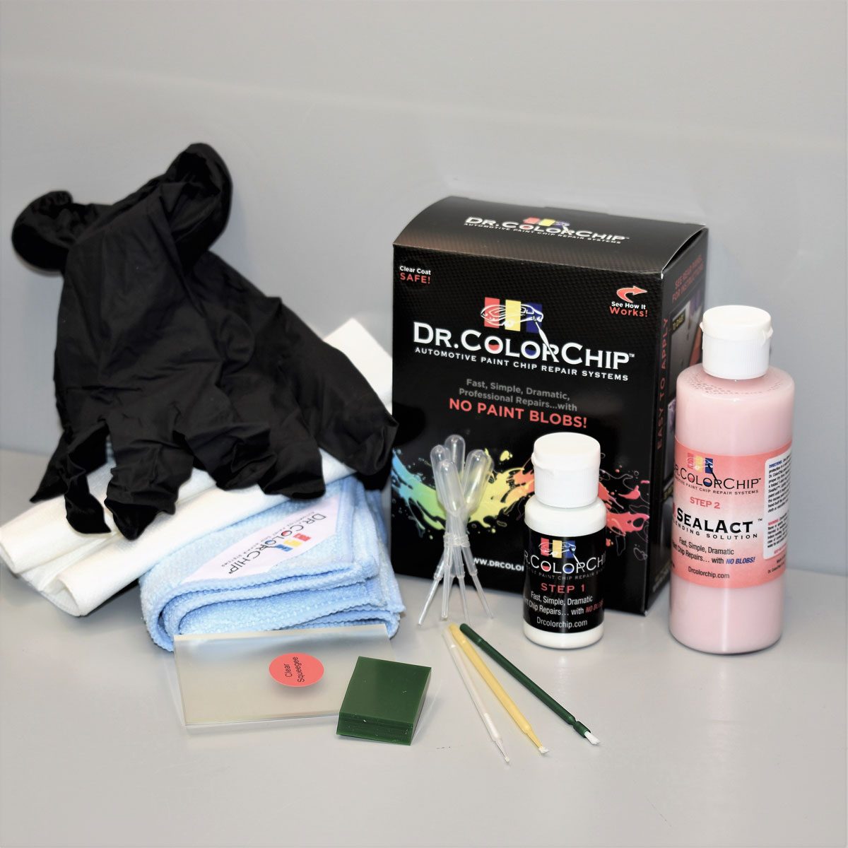 A paint chip repair kit includes gloves, cloths, solvents, and tools, arranged on a neutral surface, ready for automotive touch-up repairs.
