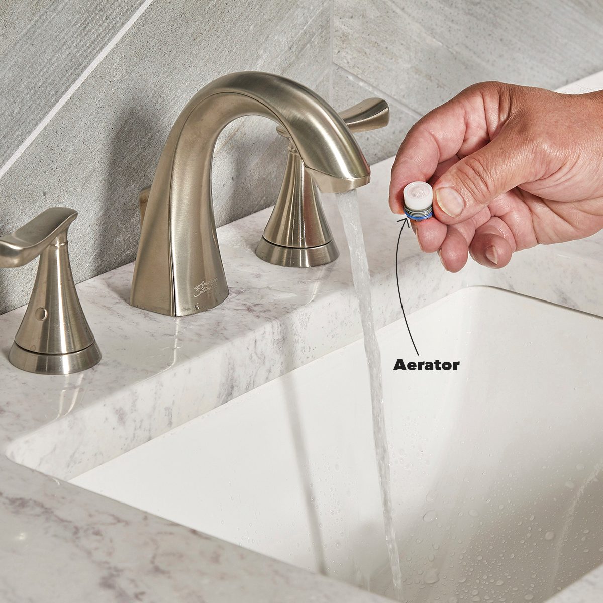 A faucet dispenses water into a sink as a hand holds an aerator, indicating a process of installation or maintenance in a bathroom setting.