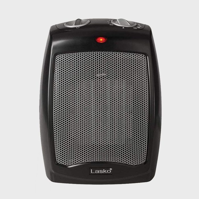 A black space heater emits heat, indicated by a red light, with control knobs on top and a mesh grill in front, suitable for indoor use.