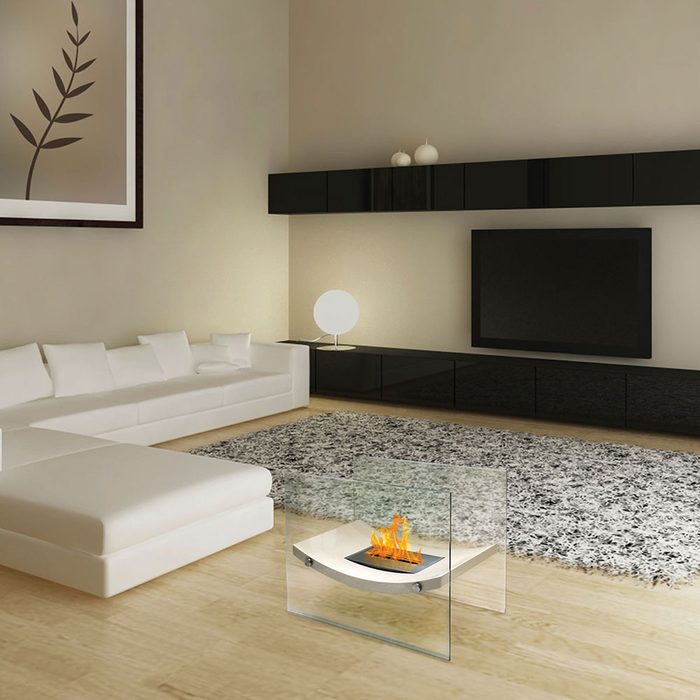 A modern coffee table with a decorative flame sits on a plush rug in a stylish living room, featuring a large sectional sofa and a sleek TV unit.