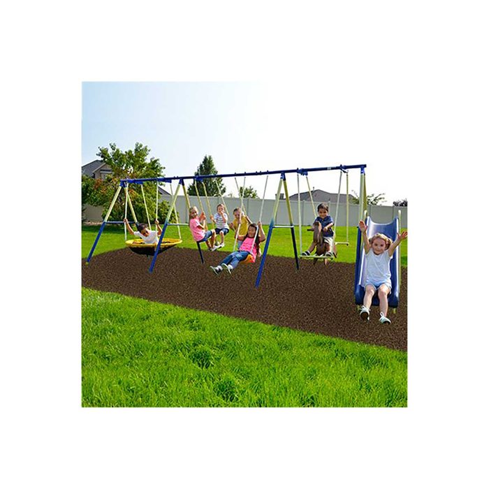 Children swing and slide joyfully on playground equipment, surrounded by grassy areas and residential homes, under a clear blue sky.