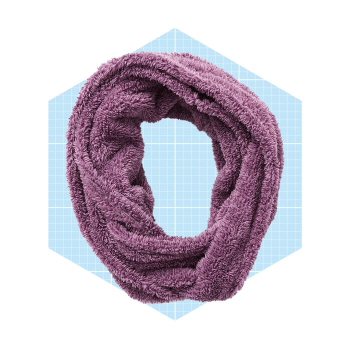 A purple infinity scarf lies twisted in a circular shape, set against a light blue geometric background with a grid pattern, suggesting a cozy accessory.