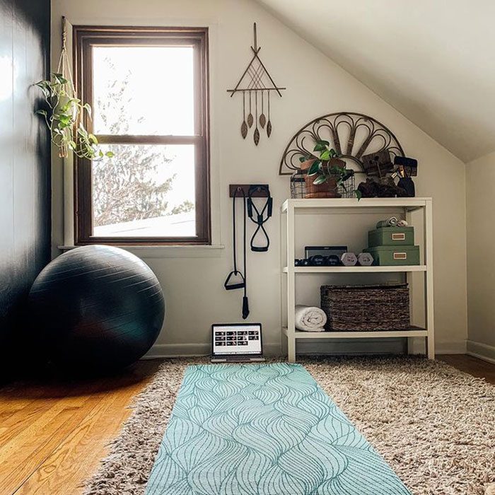 A yoga mat lies on a carpet in a well-lit room, accompanied by a fitness ball, weights, and storage, creating a calming workout environment.