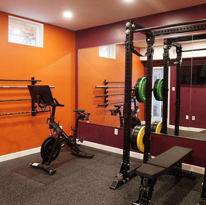 A fitness area features a stationary bike and weight rack, with green and yellow plates, surrounded by orange and purple walls and a mirror.