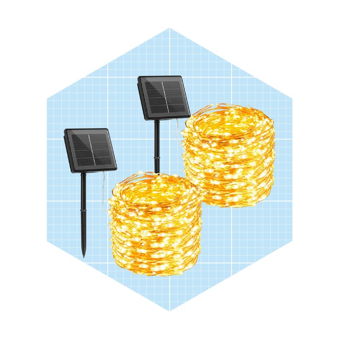 Two solar panels stand beside spirals of glowing yellow string lights against a light blue grid background. The lights appear coiled as if ready to use.
