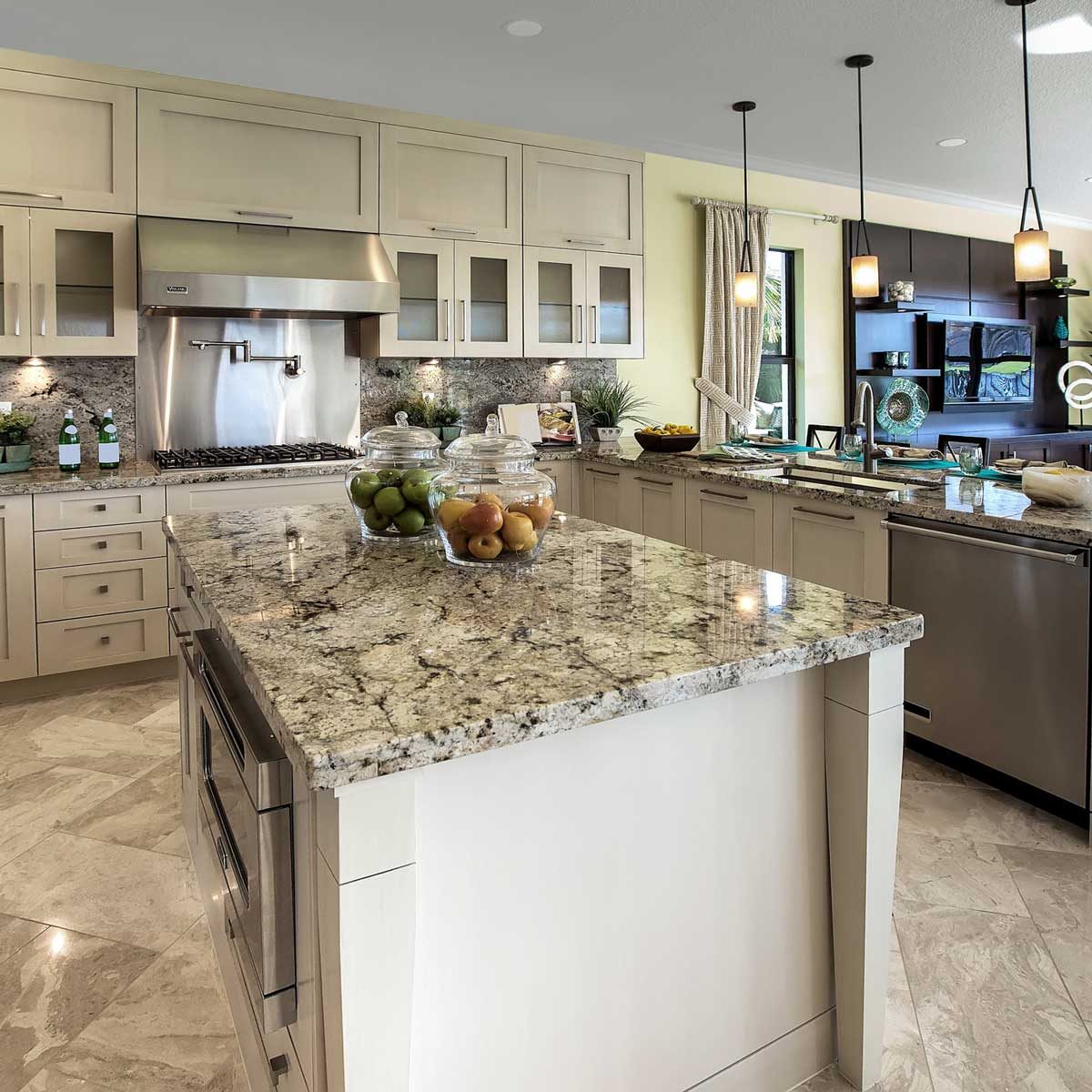 A sleek kitchen features a granite island with jars of colorful fruits, while modern appliances and cabinetry surround the cooking area in a bright, inviting space.