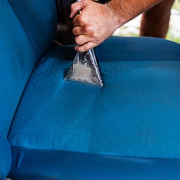 A hand holds a cleaning tool, removing dirt from a blue fabric chair cushion, situated in a casual outdoor setting.
