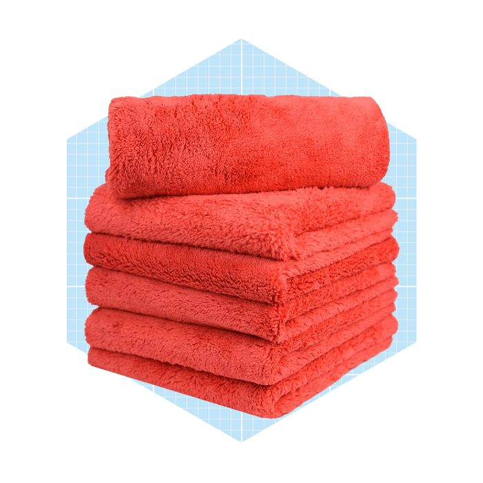 A stack of vibrant red towels rests neatly, showcasing their soft texture against a light blue grid background.