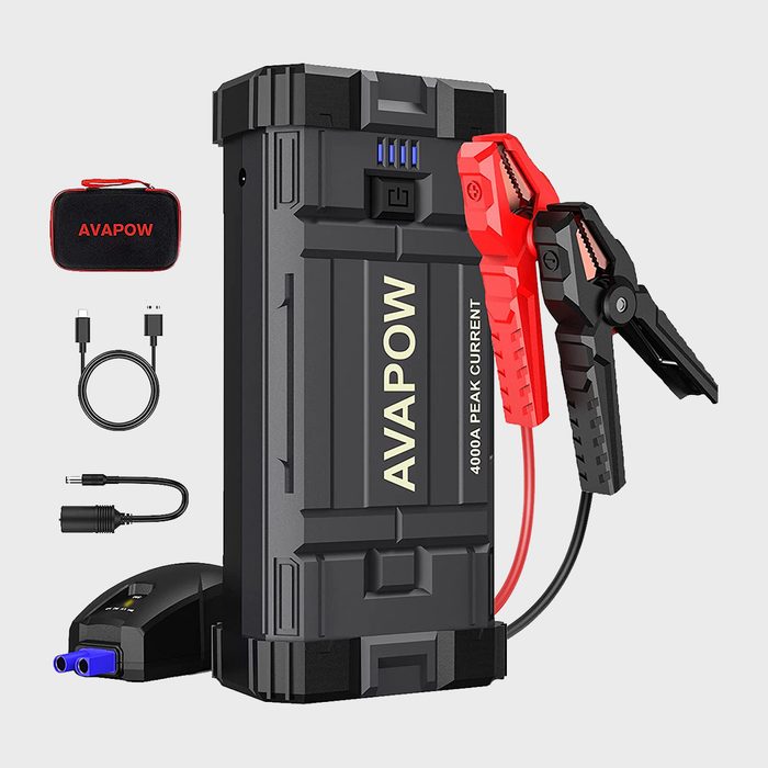 A portable jump starter, featuring red and black clamps, charges a battery, surrounded by cables and a carrying case, on a plain background.