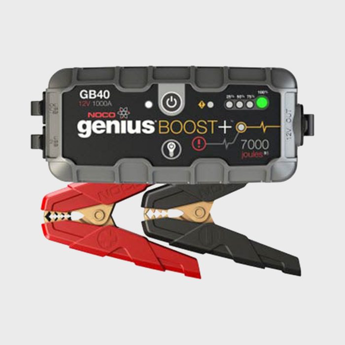 A portable jump starter with red and black clamps charges a vehicle's battery, featuring a display panel with indicators for power levels and functions.