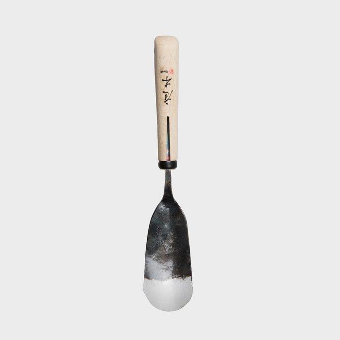 A metal trowel with a wooden handle rests upright against a plain white background, showcasing its curved blade designed for gardening or construction tasks.
