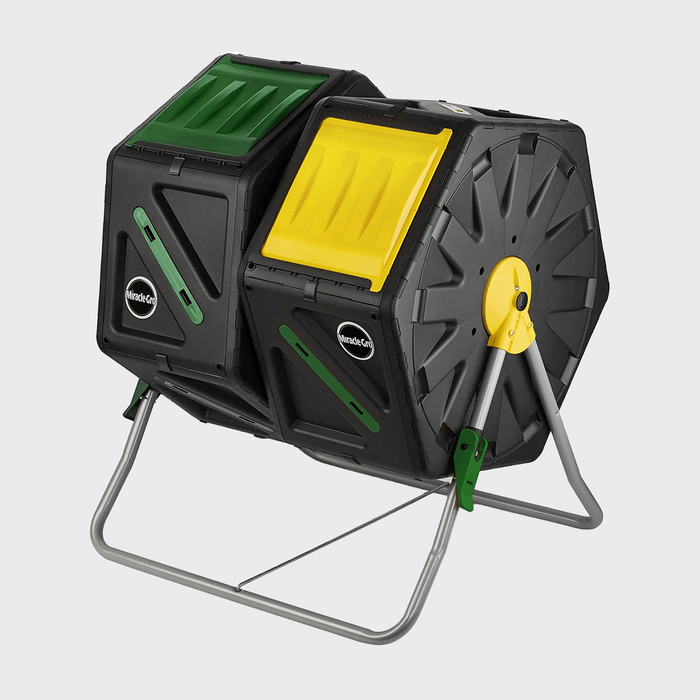 A black and yellow compost tumbler rotates on a metal frame, facilitating aerobic decomposition of organic waste in a garden or outdoor setting.