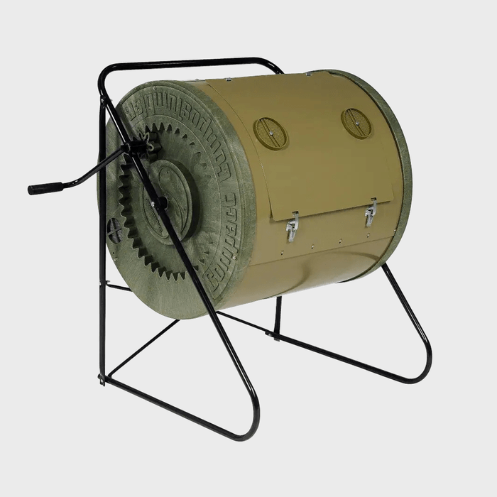 A cylindrical compost tumbler rotates manually on a sturdy black frame, allowing composting materials to mix efficiently in an outdoor garden setting.