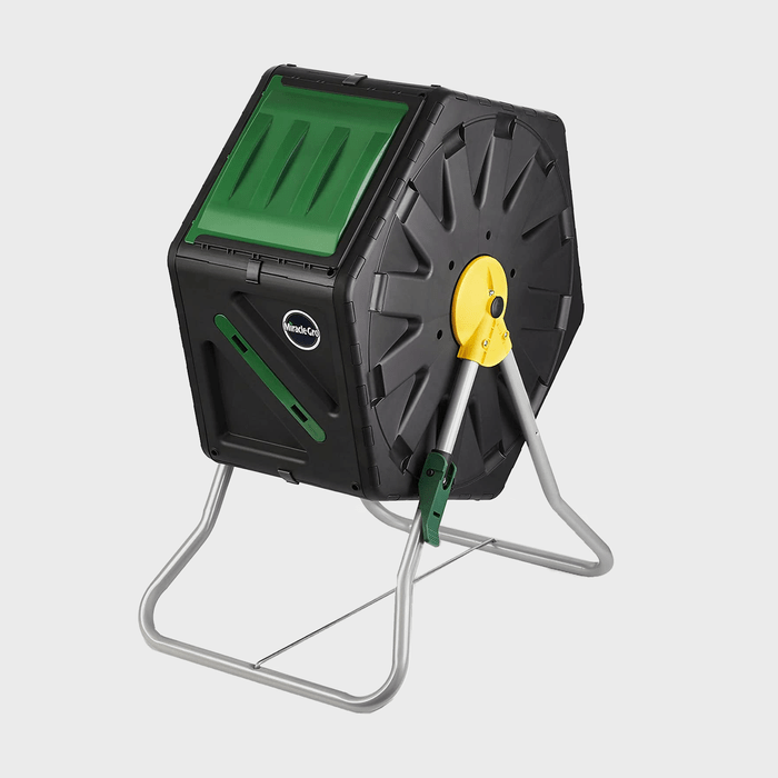 A rotating compost tumbler sits on a sturdy metal frame, designed for mixing organic waste efficiently in a garden or outdoor setting.