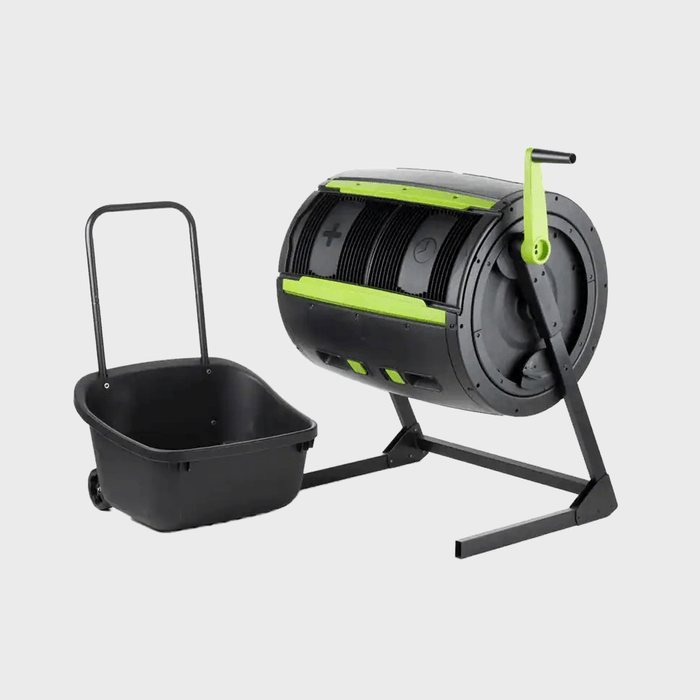 A cylindrical composter sits on a stand, with a handle for turning. Beside it is a black wheeled cart for collecting compost.