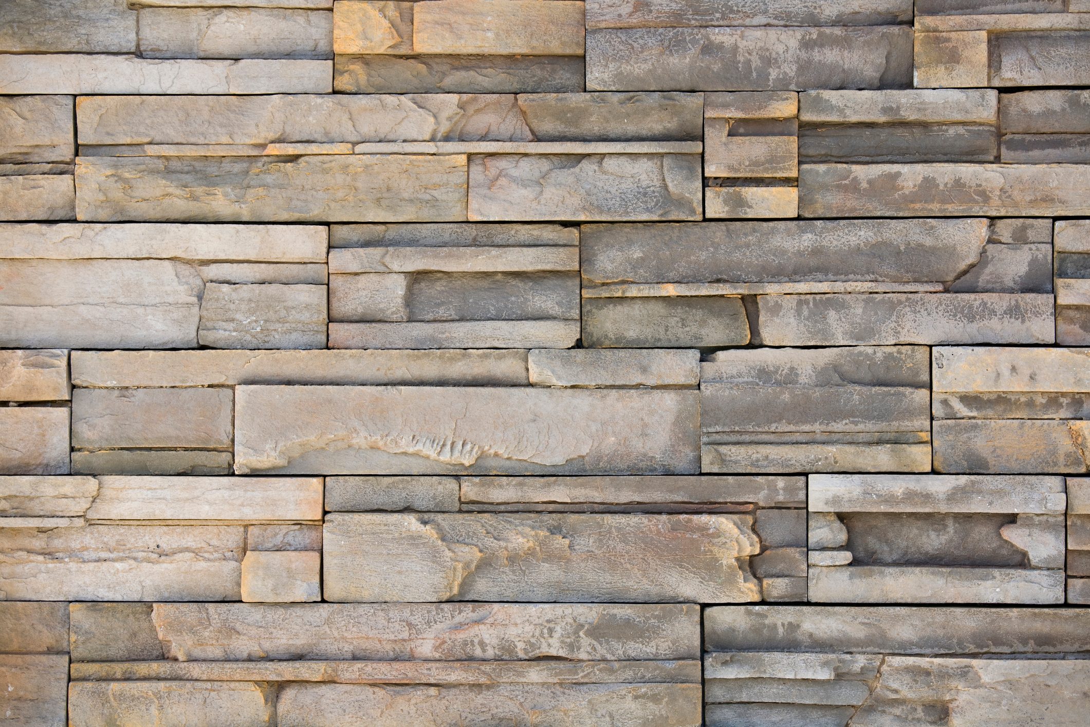 A textured stone wall displays various shapes and shades of gray, arranged in a layered pattern to create a visually appealing surface.