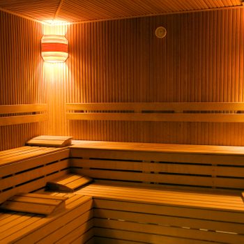 Wooden benches are arranged in a dimly lit sauna, creating a warm, relaxing atmosphere with soft lighting and a wooden-paneled design.