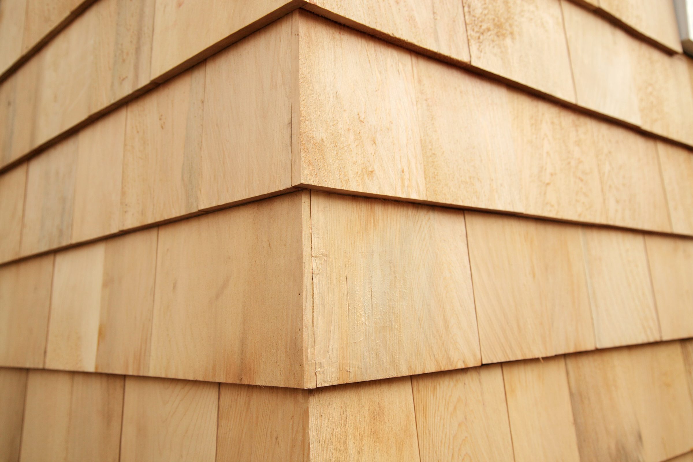 Wooden shingles stack neatly along a building's corner, creating a textured surface that blends natural materials with architectural design.