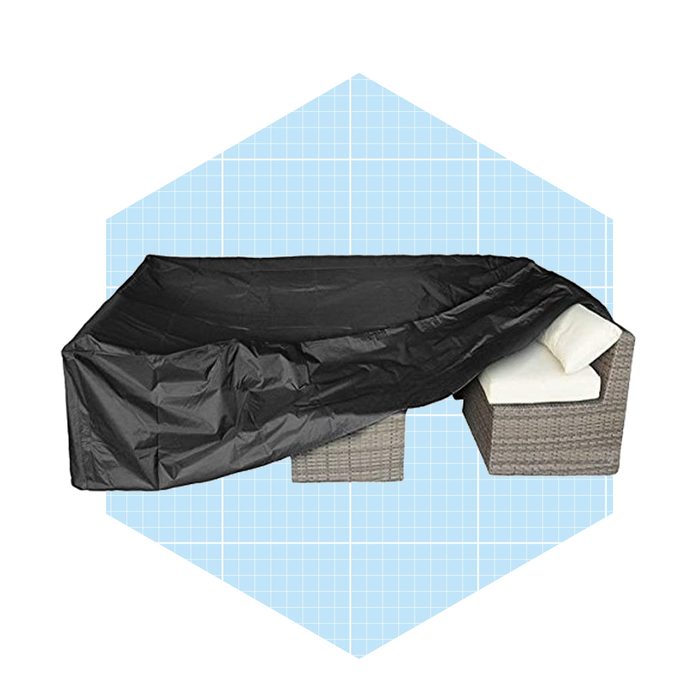 A black tarp covers two wicker chairs with cushions, protecting them, set against a light blue grid-patterned background.
