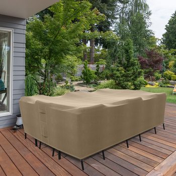 A beige outdoor furniture cover rests on a deck, protecting a couch. Lush greenery and a well-maintained garden create a serene backyard environment.