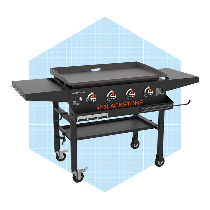 A large, black griddle with three control knobs is set on a wheeled cart against a light blue geometric background.