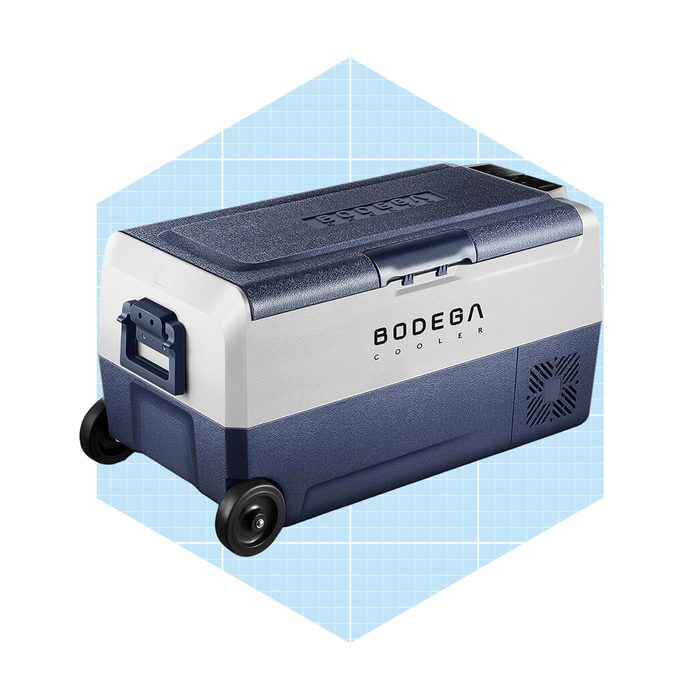 A blue and white cooler is positioned on a light grid background, featuring wheels for mobility and a latch for securing the lid.