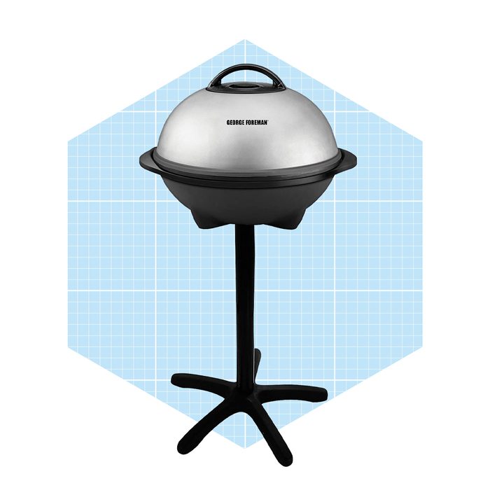 A round electric grill stands on a black tripod base. It features a shiny silver dome-shaped lid and a textured black grilling surface against a pale blue grid background.